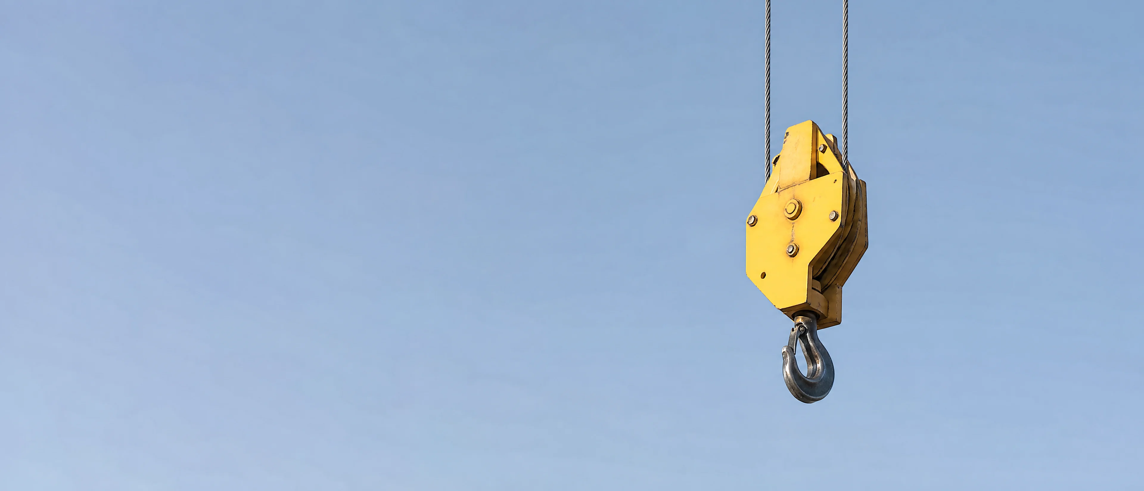 Gelber Kranhaken an einem Stahlseil vor blauem Himmel